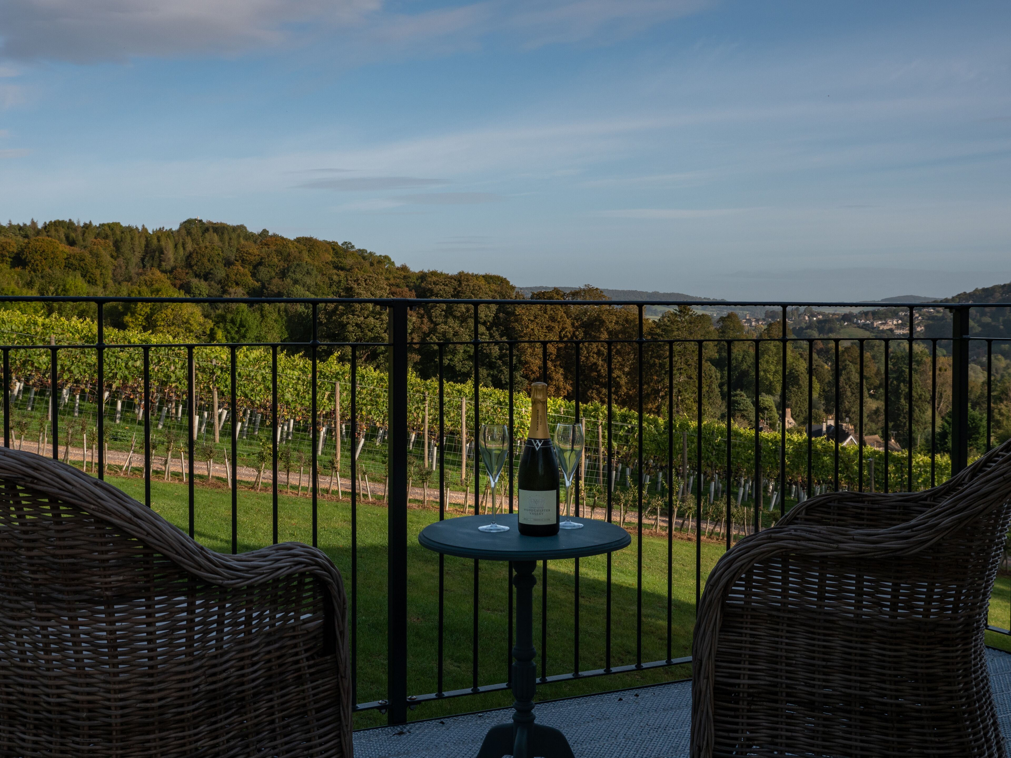 A balcony with wicker chairs, a table, and a bottle of wine.