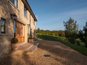A stone building with a large wooden door, potted plants, and a gravel driveway leading to a vineyard. - Woodchester Valley House (Stroud)