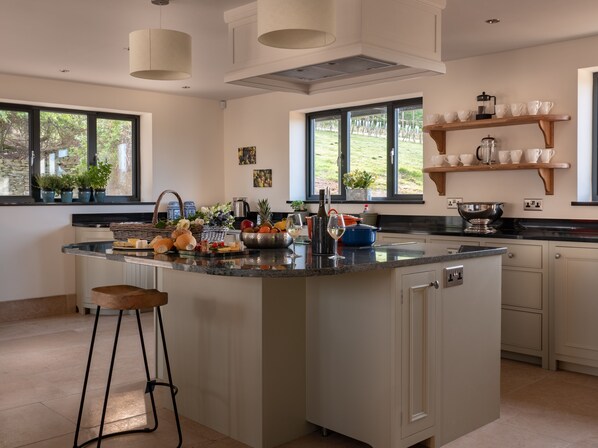 A modern kitchen with a large island, built-in appliances, and a view of the garden. - Woodchester Valley House (Stroud)