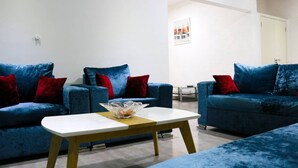 A modern living room with two blue sofas, a white coffee table, and red cushions.