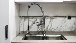 A kitchen with a single stainless steel sink, a flexible faucet, and a marble backsplash.