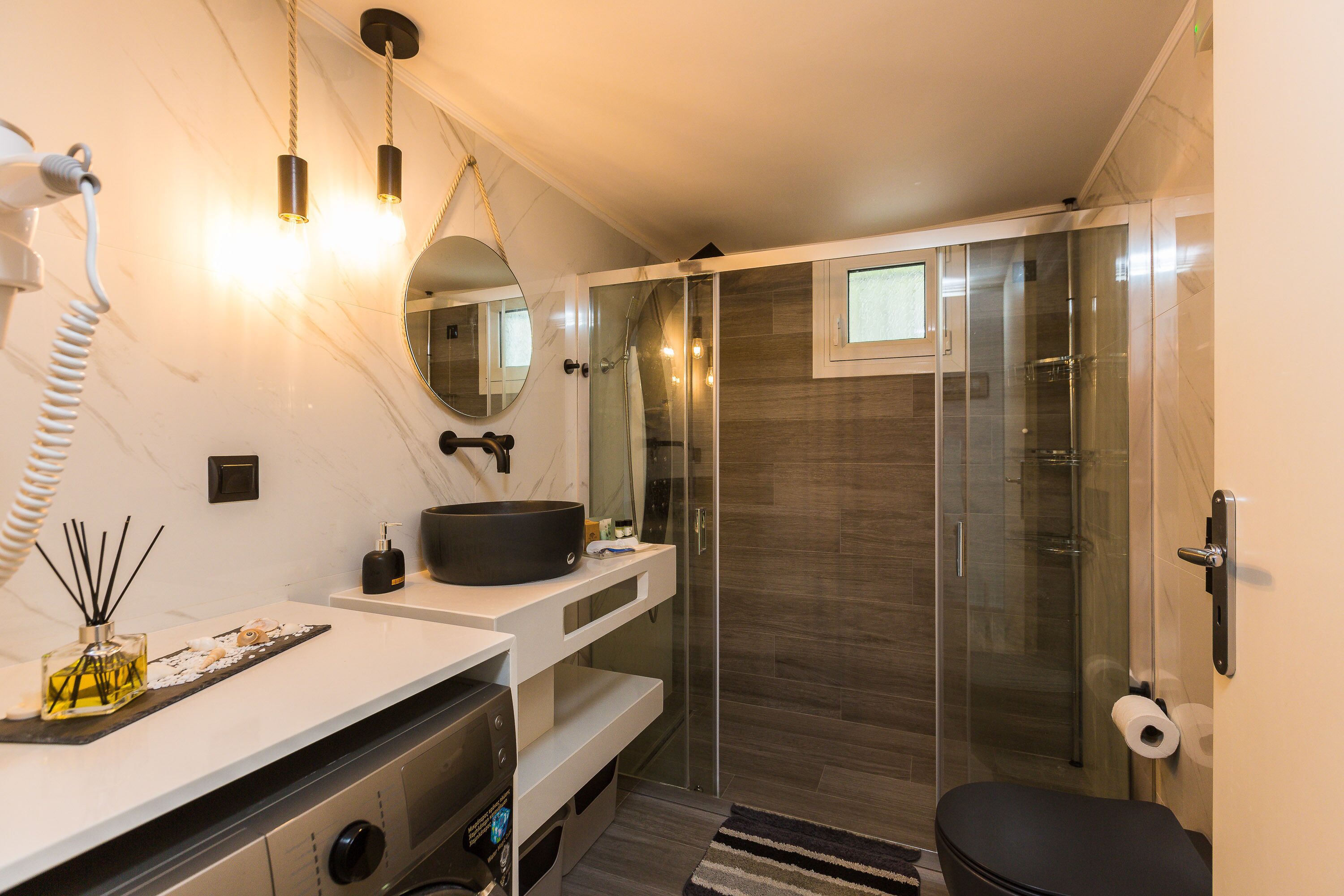 A modern bathroom with a glass shower enclosure, a white vanity with a black sink, and a mirror above the vanity.