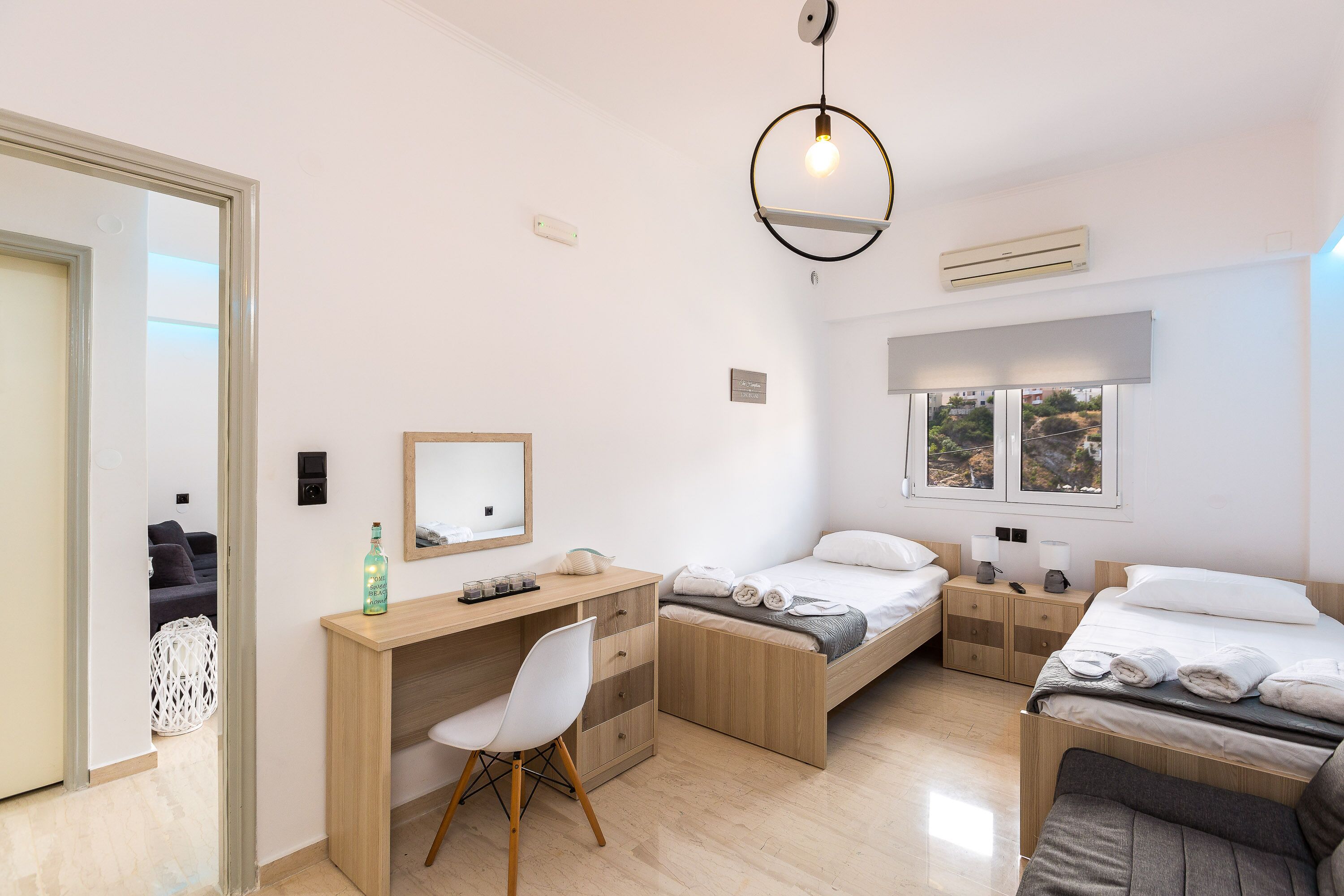 A modern bedroom with a desk, two beds, a chair, and a large window.