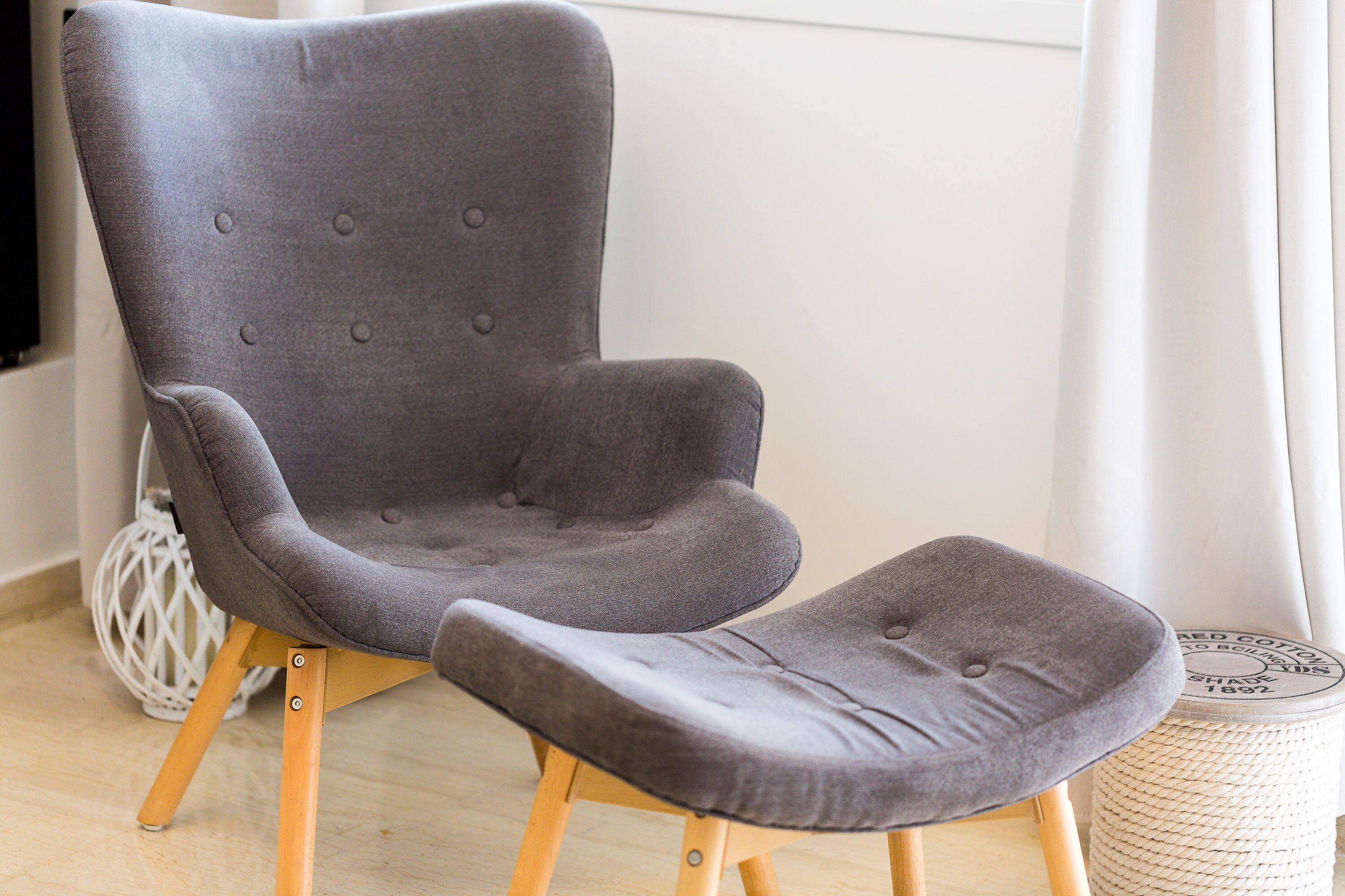 A grey upholstered armchair with wooden legs and a matching ottoman.