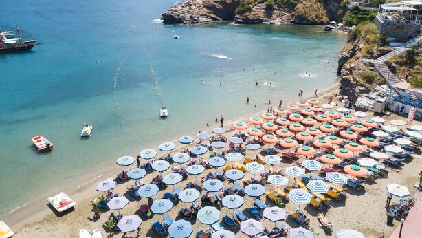 A beach with numerous umbrellas and sun loungers, boats in the water, and buildings on the hillside. - Ocean Dream Suite (Mylopotamos)