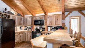 A kitchen with wooden cabinets, a black refrigerator, a microwave, and a wooden dining table with chairs. - Spring Haven Home: Gorgeous, Dog Friendly (Breckenridge)