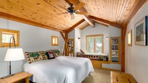 A cozy bedroom with a large bed, a wooden ceiling fan, a bookshelf, and a window with a view of the outdoors. - Spring Haven Home: Gorgeous, Dog Friendly (Breckenridge)