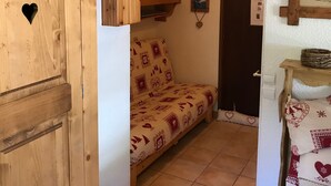 A cozy room with a wooden cabinet, a sofa with patterned upholstery, a wall-mounted shelf with decorative items, and a door with a heart-shaped cutout. - Accommodation at the foot of the ski slopes (La Giettaz)