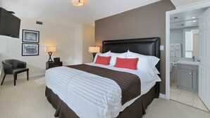 Une chambre d’hôtel avec un grand lit, deux lampes de chevet, un téléviseur à écran plat, une chaise et une salle de bain visible à travers une porte ouverte.