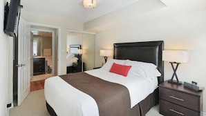 Une chambre d’hôtel dotée d’un grand lit, de lampes de chevet, d’un téléviseur à écran plat fixé au mur et d’une porte donnant accès à une salle de bain.