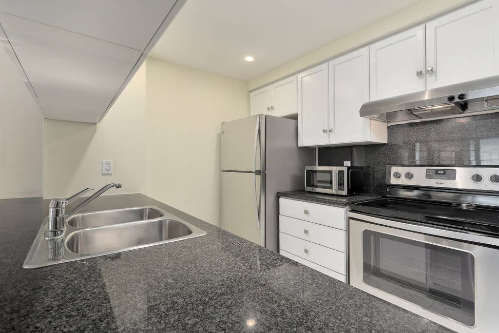 A compact kitchen with a stainless steel refrigerator, a microwave, an oven, and a double sink.