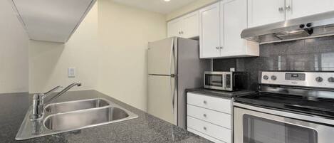 Una cocina compacta con refrigerador de acero inoxidable, microondas, horno y pileta doble.