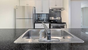 Une cuisine moderne dotée d’appareils électroménagers en acier inoxydable, d’un plan de travail en granit et de meubles blancs.