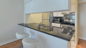 Une cuisine compacte avec des meubles blancs, un plan de travail noir, un évier à deux bacs et un four encastré.