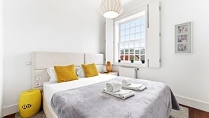 A modern hotel room with a bed, a window with a view, a bedside table, and a yellow ottoman. - GuestReady - Ribeira retreat in Porto centre (Porto)