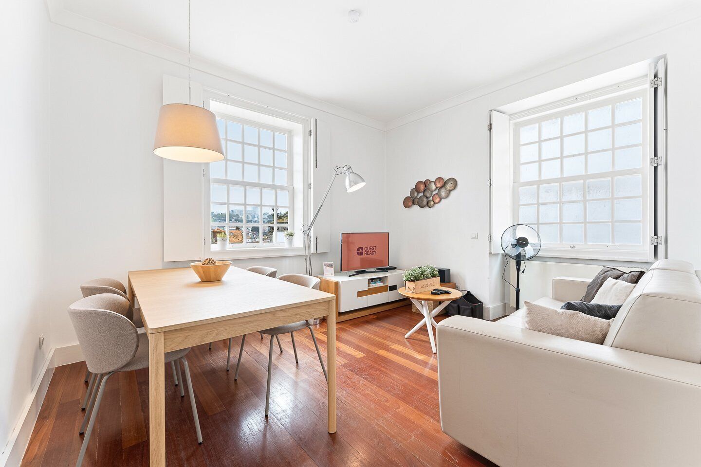 A modern living room with a wooden dining table, a sofa, a TV, and a large window.