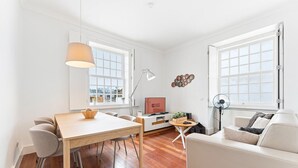 A modern living room with a wooden dining table, a sofa, a TV, and a large window. - GuestReady - Ribeira retreat in Porto centre (Porto)