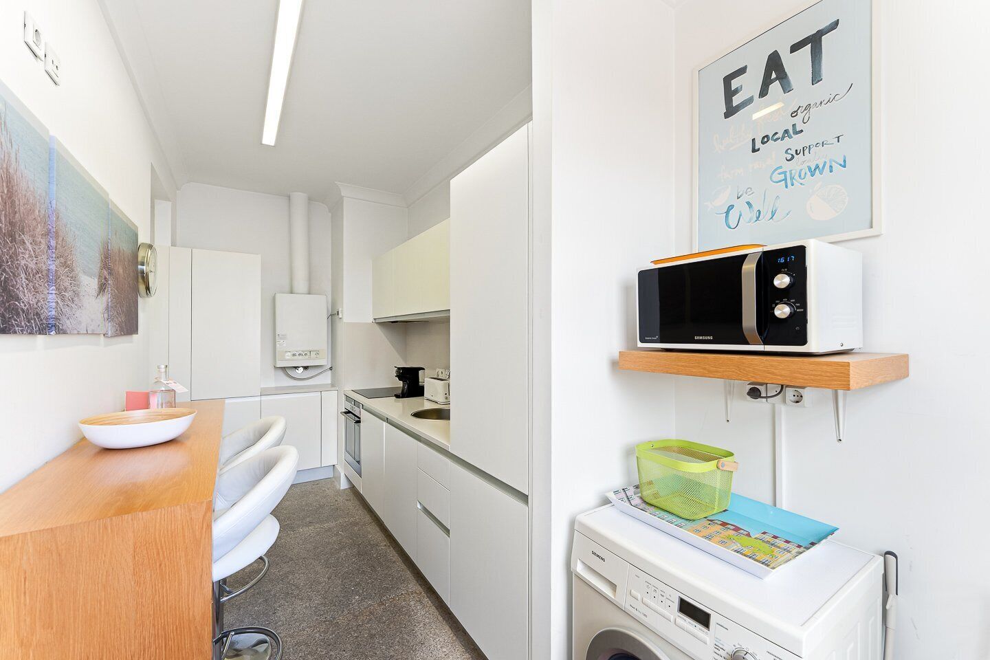 A modern kitchen with white cabinetry, a microwave, a washing machine, and a sink.