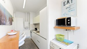 A modern kitchen with white cabinetry, a microwave, a washing machine, and a sink. - GuestReady - Ribeira retreat in Porto centre (Porto)