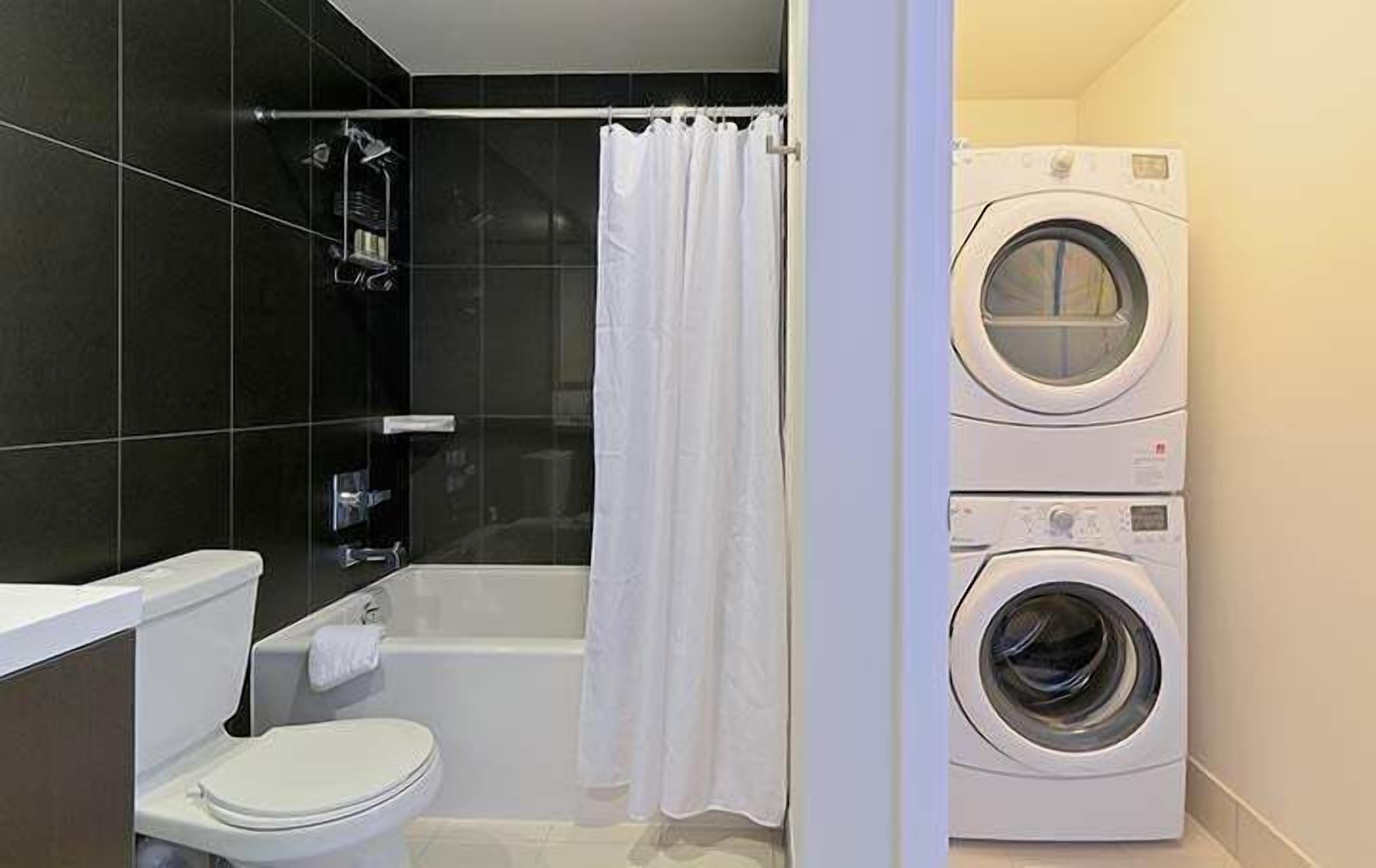 Une petite salle de bain comprenant des toilettes, une baignoire et un lave-linge et un sèche-linge superposés.