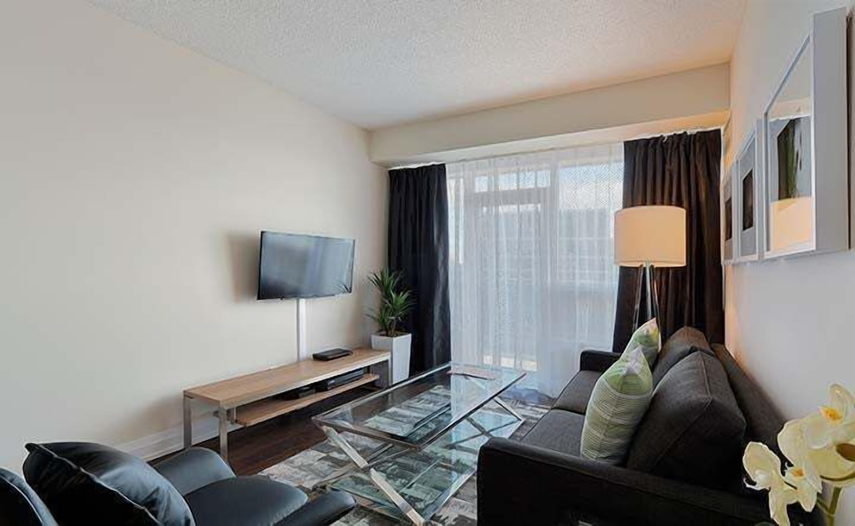 A modern living room with a glass coffee table, leather sofa, and a flat-screen TV mounted on the wall.
