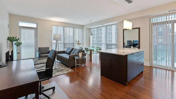 A spacious living area with a large island, a sofa, a dining table, and a TV. - 2 Bedroom/2 Bathroom Deluxe Suite (Toronto)