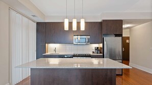 A modern kitchen with dark wood cabinets, a central island, stainless steel appliances, and pendant lighting. - 2 Bedroom/2 Bathroom Deluxe Suite (Toronto)