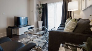 A modern living room with a flat-screen TV, a glass coffee table, a sofa, and a floor lamp. - 1 Bedroom/1 Bathroom Suite (Toronto)