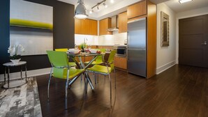 A modern kitchen with wooden cabinets, stainless steel appliances, and a dining area with green chairs and a glass table. - 1 Bedroom/1 Bathroom Suite (Toronto)