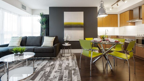 A modern living space with a dining area, a kitchen, and a grey sofa with a small table and plants. - 1 Bedroom/1 Bathroom Suite (Toronto)