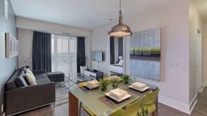 A modern living room with a sofa, a dining table set for four, and a TV in the background. - 2 Bedroom/2 Bathroom Suite (Toronto)