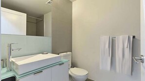A modern bathroom with a glass-topped sink, a white toilet, and a towel rack on the wall. - 2 Bedroom/2 Bathroom Suite (Toronto)