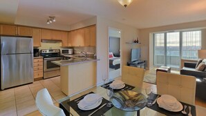 A modern kitchen with stainless steel appliances, a dining area with a glass table, and a balcony with a city view. - 2 Bedroom/2 Bathroom Suite (Scarborough ON)