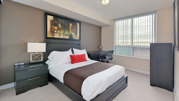 A hotel room with a bed, a desk, a chair, a nightstand, a lamp, a painting, and a window with blinds. - 2 Bedroom/2 Bathroom Suite (Scarborough ON)