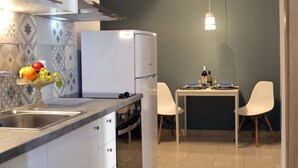 A modern kitchen with white cabinets, a built-in oven, and a dining area with two white chairs and a table. - Stylish Modern Apartment (Thessaloniki)