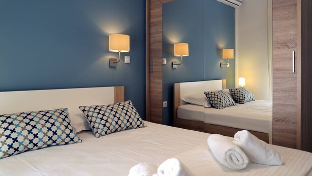 A hotel room with a large bed, two patterned pillows, a mirror, and a wall-mounted air conditioner. - Stylish Modern Apartment (Thessaloniki)