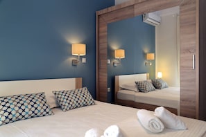 Habitación de hotel con una cama grande, dos almohadas estampadas, un espejo y un aire acondicionado de pared.