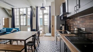 A modern kitchen with a brick backsplash, a dining area with a wooden table and chairs, and a blue sofa in a bright living space with large windows. - PHILIPPE AUGUSTE LOFT 2 - Loft for 10 - 4 rooms - BASTILLE - PÈRE LACHAISE (Paris)