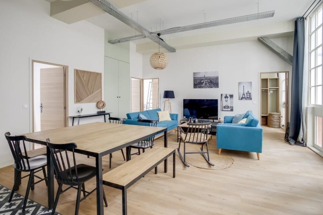 A modern living room with a wooden dining table, blue sofas, and a TV.