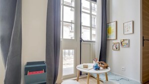 A room with a large window, a small table with toys, a blue storage unit, and a blue cushion on the floor. - PHILIPPE AUGUSTE LOFT 2 - Loft for 10 - 4 rooms - BASTILLE - PÈRE LACHAISE (Paris)