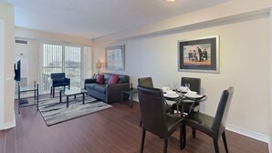 Een moderne woonkamer met een bank, een eettafel voor vier personen en een televisie.