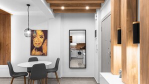 A modern kitchen with wooden beams, a dining area with a round table and chairs, and a large artwork on the wall. - White and Wood Nilie Hospitality MGMT (Thessaloniki)