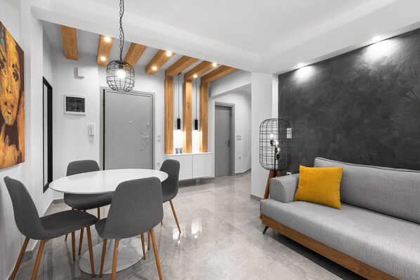 A modern living room with a grey sofa, a round dining table with four chairs, and a large abstract painting on the wall. - White and Wood Nilie Hospitality MGMT (Thessaloniki)