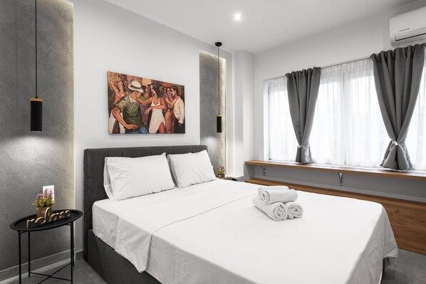 Una habitación de hotel moderna con una cama grande, un cuadro en la pared, una mesita con una planta y una ventana con cortinas.