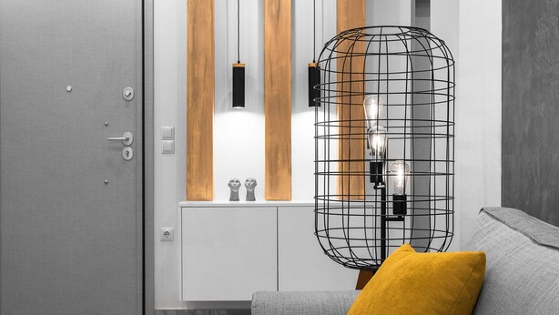 A modern living room with a grey sofa, a mustard yellow pillow, a white cabinet, and a black wireframe lamp. - White and Wood Nilie Hospitality MGMT (Thessaloniki)