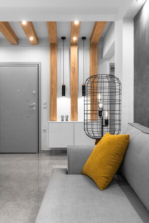 Una sala moderna con un sofá gris, un cojín amarillo mostaza, un mueble blanco y una lámpara de alambre negra.