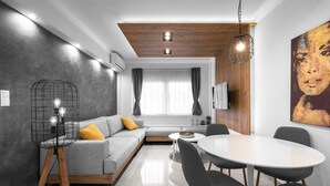 A modern living room with a grey sofa, wooden accents, a dining table with chairs, and a large painting on the wall. - White and Wood Nilie Hospitality MGMT (Thessaloniki)