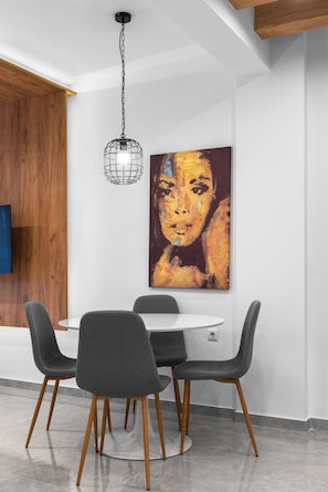 A dining area with a round table, four chairs, a pendant light, and a large painting on the wall.