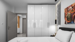 A modern hotel room with a large bed, white linens, a wardrobe with sliding doors, a painting on the wall, and a nightstand with a lamp. - White and Wood Nilie Hospitality MGMT (Thessaloniki)
