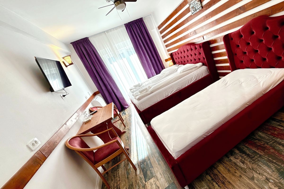 Een hotelkamer met twee bedden, een bureau, een stoel, een televisie en een raam met gordijnen.